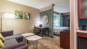 A hotel room with a sofa, a small desk, a bed, a mirror, and artwork on the wall.