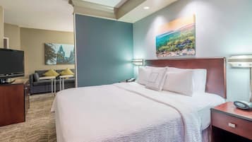 Habitación de hotel con una cama grande, un escritorio con televisor de pantalla plana, un sofá con cojines y obras de arte en las paredes.