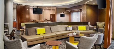 A modern lounge area with a sofa, armchairs, a coffee table, and a TV mounted on the wall.