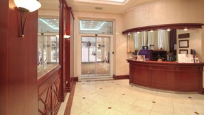 A reception area with a wooden reception desk, a glass door leading outside, and a ceiling with recessed lighting. - Hotel Orasac (Belgrade)