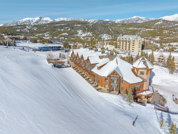 Un centro de esquí con un gran refugio, pistas cubiertas de nieve y vistas a las montañas.