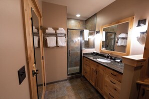A modern bathroom with a glass shower, a large mirror, and wooden cabinets. - The Village Center at Big Sky Resort (Big Sky)