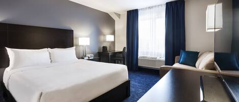 A hotel room with a large bed, a desk, a chair, a desk lamp, a desk lamp, a chair, a desk lamp, a chair, a desk lamp, a chair, a desk lamp, a chair, a desk lamp, a chair, a desk lamp, a chair, a desk lamp, a chair, a desk lamp, a chair, a desk lamp, a chair, a desk lamp, a chair, a desk lamp, a chair, a desk lamp, a chair, a desk lamp, a chair, a desk lamp, a chair, a desk lamp, a chair, a desk lamp, a chair, a desk lamp, a chair, a desk lamp, a chair, a desk lamp, a chair, a desk lamp, a chair, a desk lamp, a chair, a desk lamp, a chair, a desk lamp, a chair, a desk lamp, a chair, a desk lamp, a chair, a desk lamp,