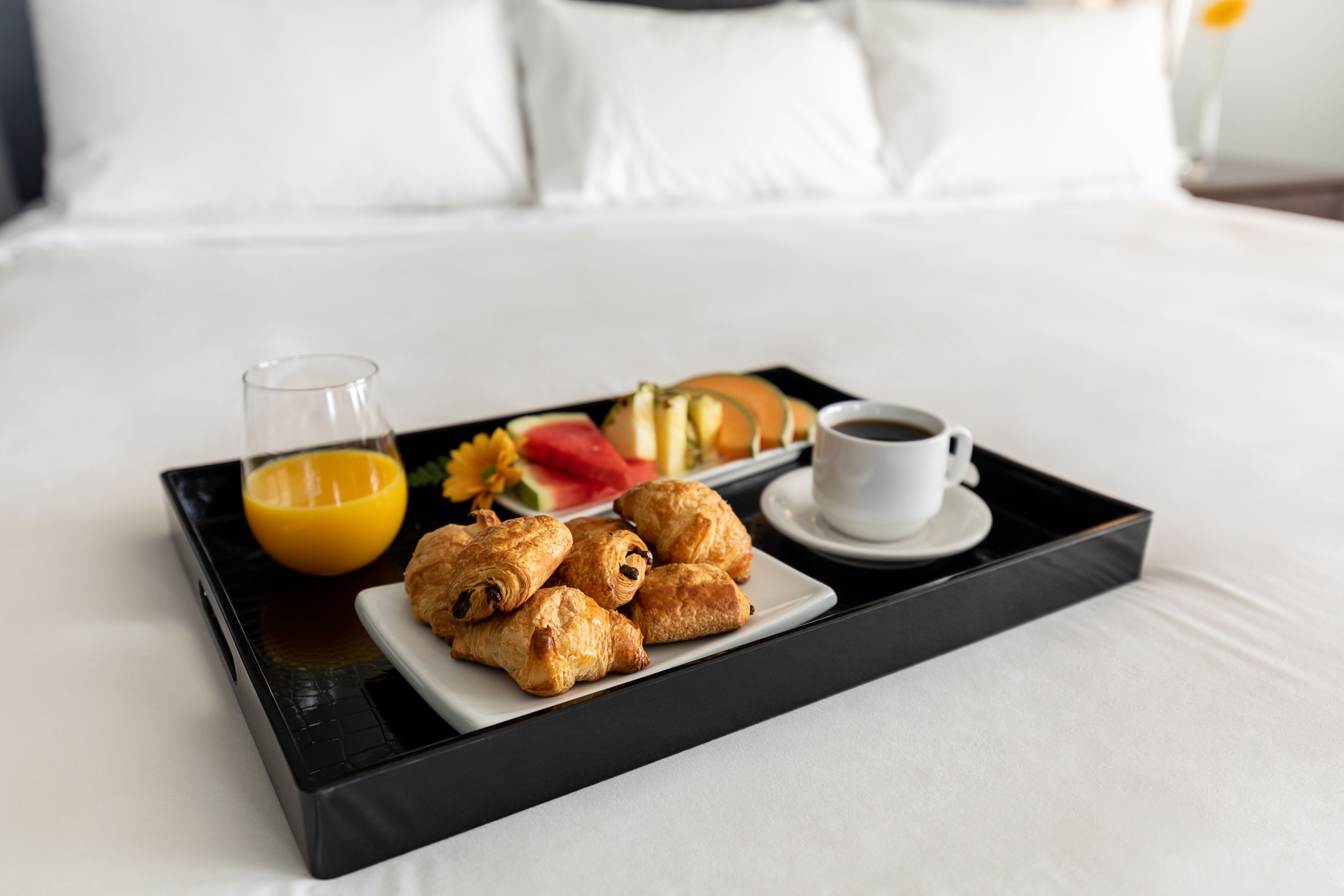 A tray with pastries, a glass of orange juice, and a cup of coffee on a bed.