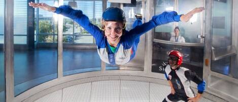 An indoor skydiving facility with a large open space and a glass wall providing a view of the outside.
