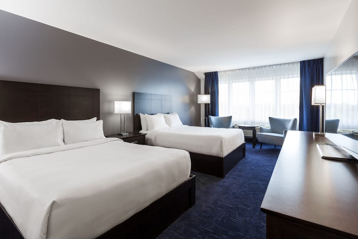A hotel room with two beds, a desk, and a chair.