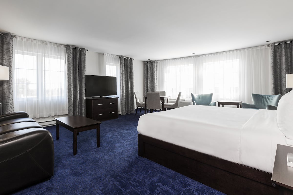 A hotel room with a large bed, a desk, a TV, and a seating area with chairs.