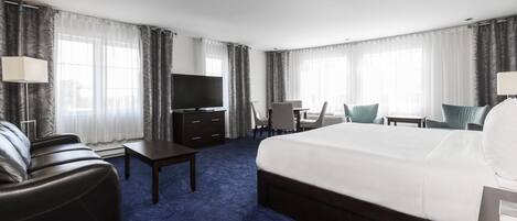 A hotel room with a large bed, a desk, a TV, and a seating area with chairs.