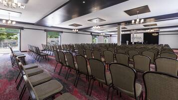 Une salle de conférence avec des rangées de chaises, une scène et un lustre.