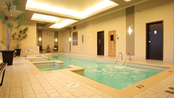 Piscina com piso ladrilhado e teto com iluminação embutida. Há portas e um relógio na parede.