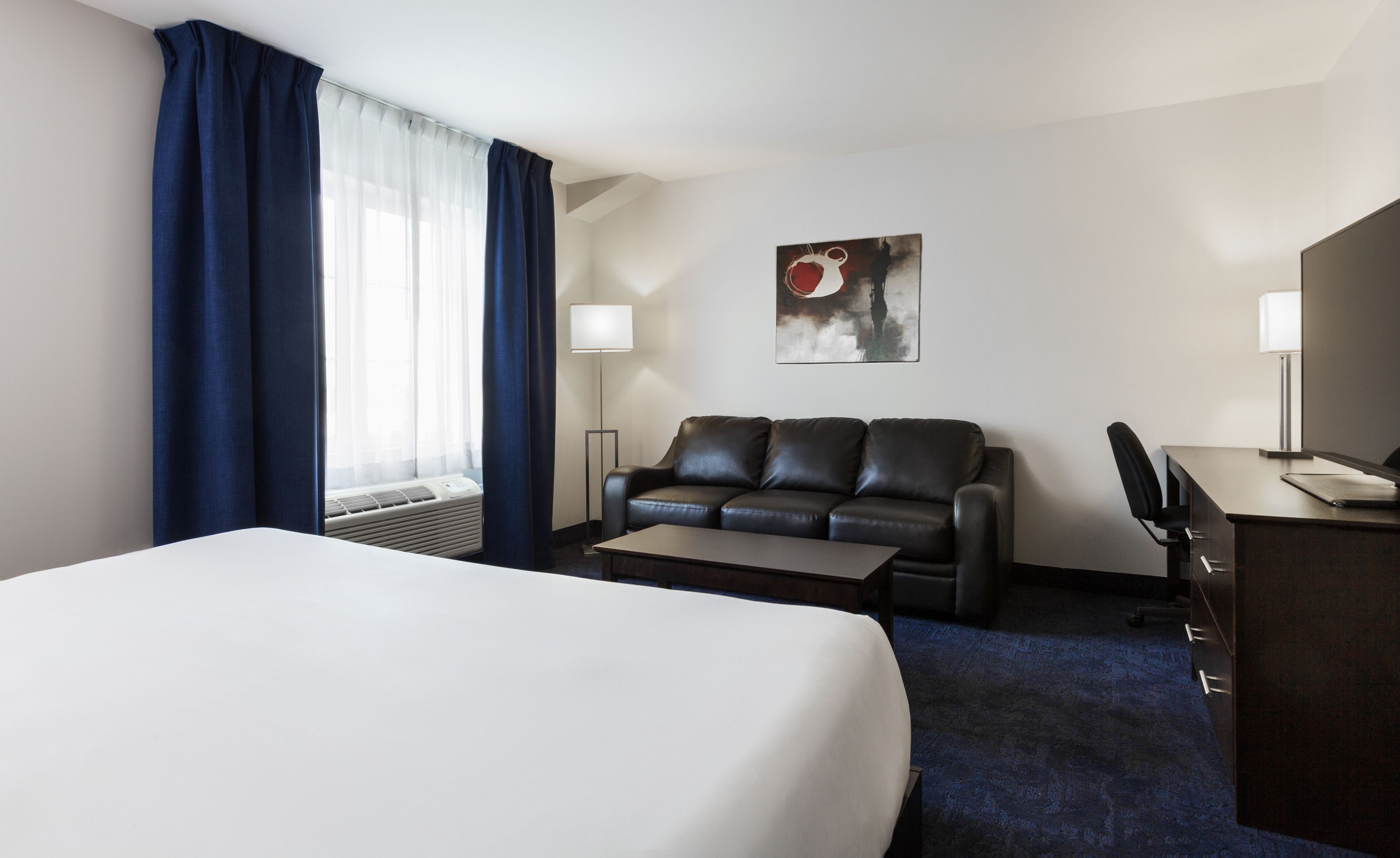 A hotel room with a large bed, a black leather sofa, a desk, and a lamp.
