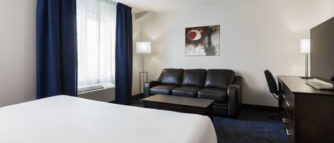 A hotel room with a large bed, a black leather sofa, a desk, and a lamp.