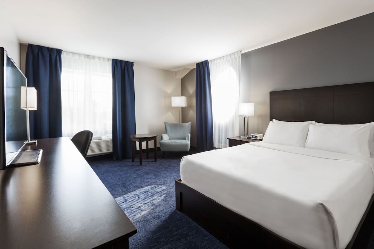 A hotel room with a large bed, a desk, a chair, and a small table.