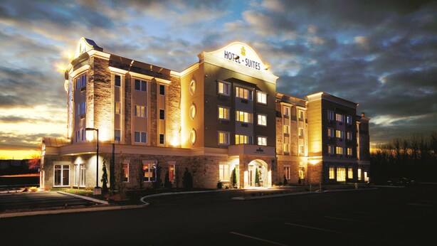 A hotel with a prominent "HOTEL SUITES" sign, multiple floors, and a well-lit entrance. - Imperia Hotel and Suites (Saint-Eustache)