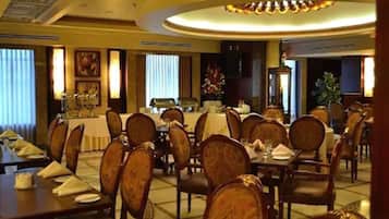 A dining area with multiple tables and chairs, a central buffet, and a chandelier.