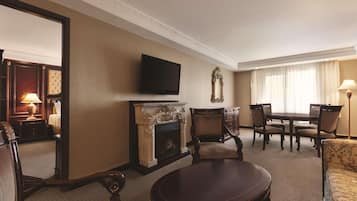 Een hotelkamer met een open haard, een aan de muur bevestigde televisie, een eettafel met stoelen en een bank.