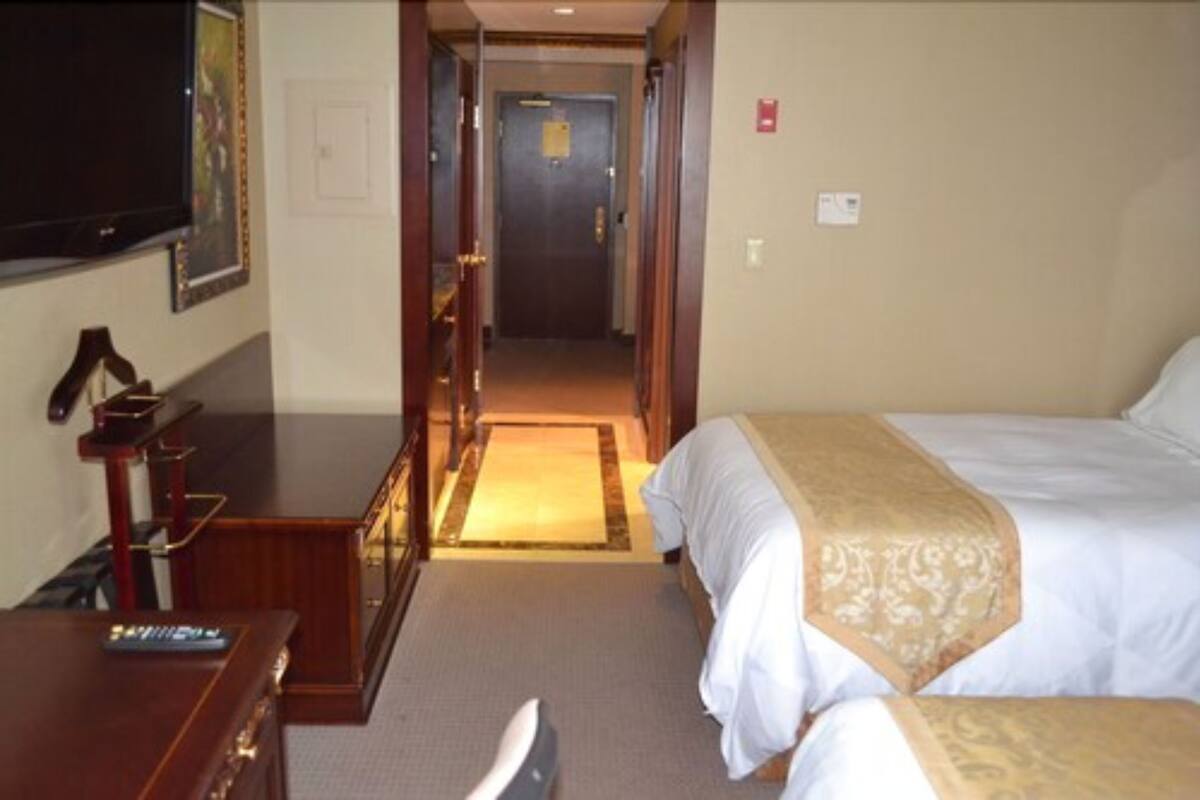 A hotel room with a bed, a desk, a television, and a door leading to another room.