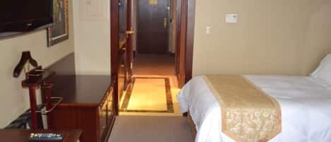 A hotel room with a bed, a desk, a television, and a door leading to another room.