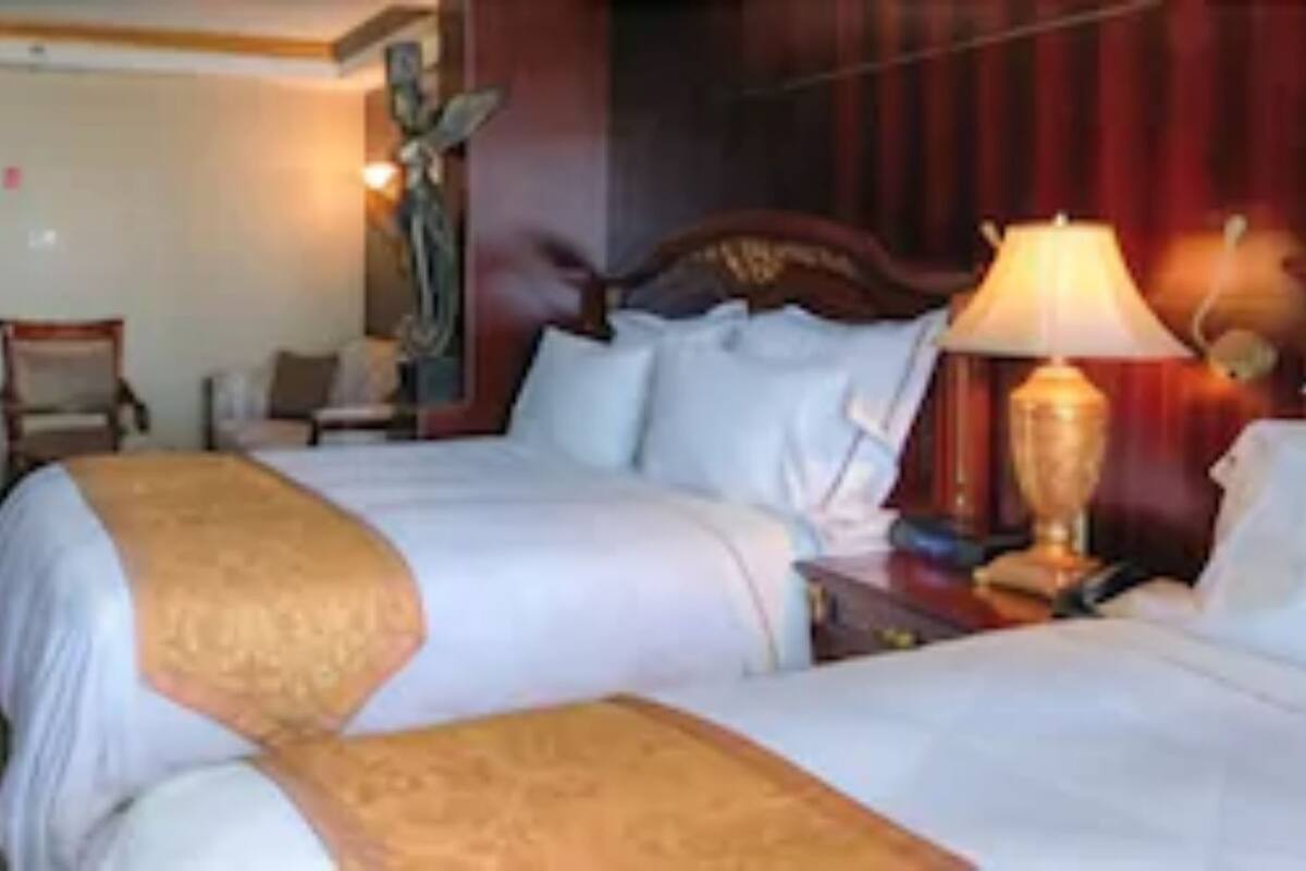 A hotel room with two beds, a wooden headboard, a nightstand with a lamp, and a chair.