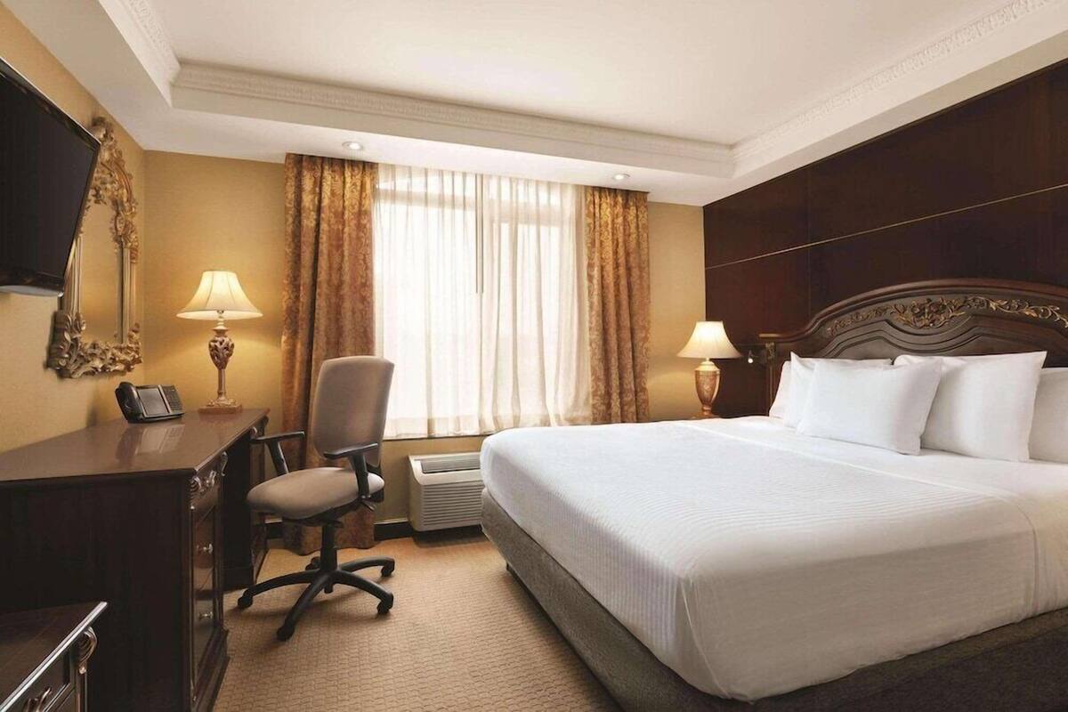 A hotel room with a large bed, a desk with a telephone, a chair, two lamps, and a large mirror on the wall.