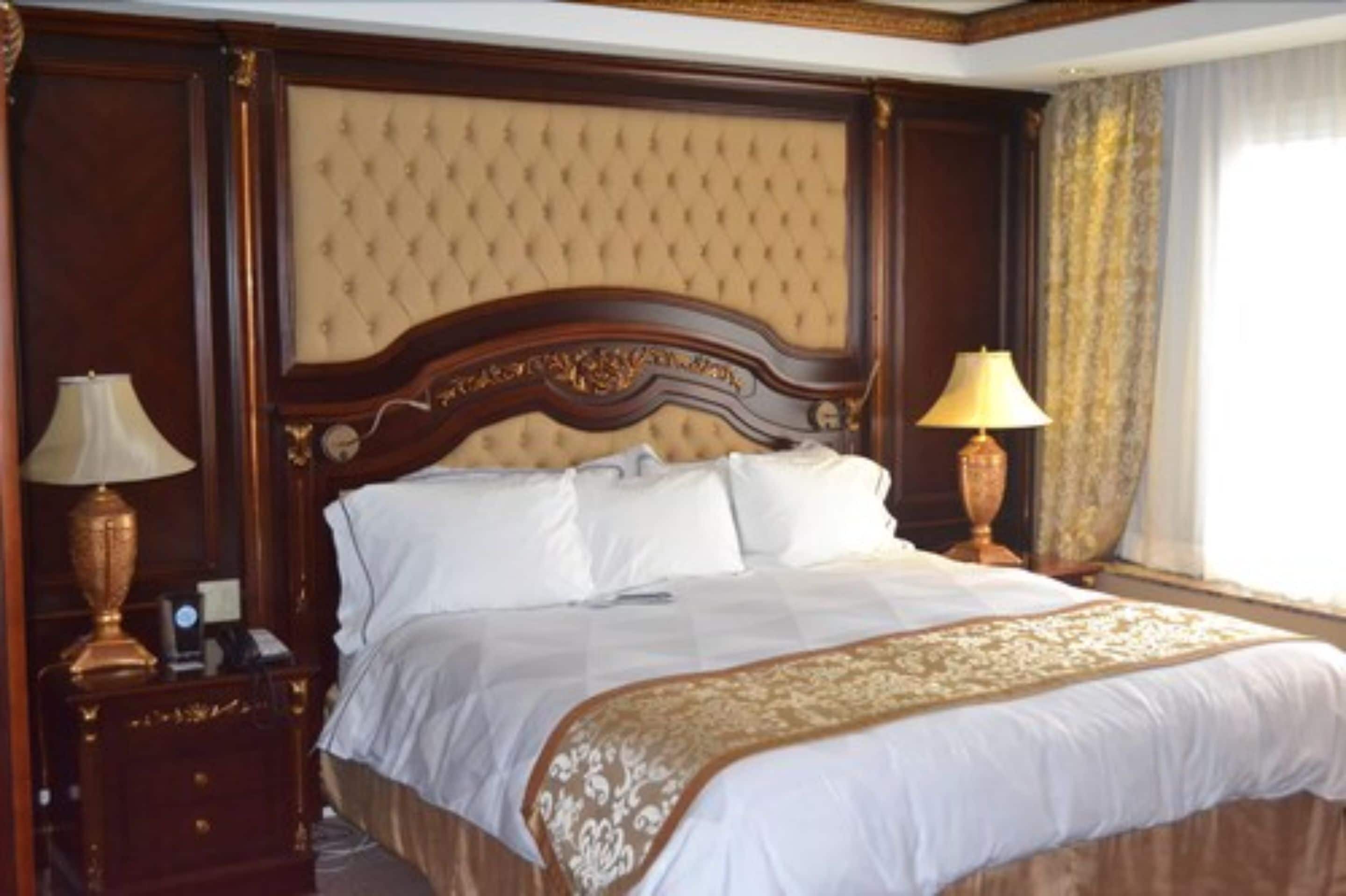 A large bed with a tufted headboard, two bedside lamps, and a decorative bedspread.