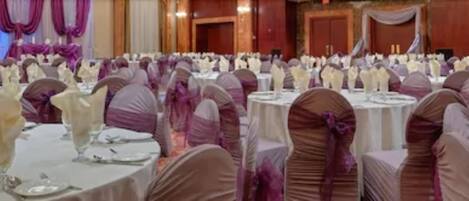Une salle de banquet avec des tables rondes dressées pour un événement formel, décorées de nappes blanches et de rubans violets.