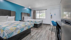 Quarto de hotel com duas camas, uma mesa, uma cadeira e uma janela grande.
