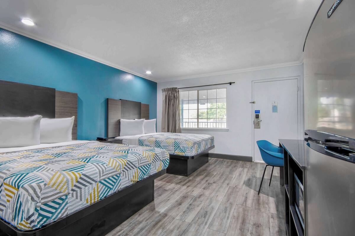 A hotel room with two beds, a desk, a chair, and a large window.