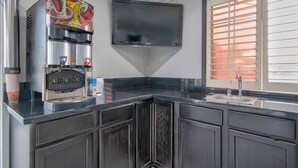 A modern kitchen with a built-in coffee maker, a flat-screen TV, and a window with blinds. - Studio 6 Suites – San Bernardino, CA  (San Bernardino)