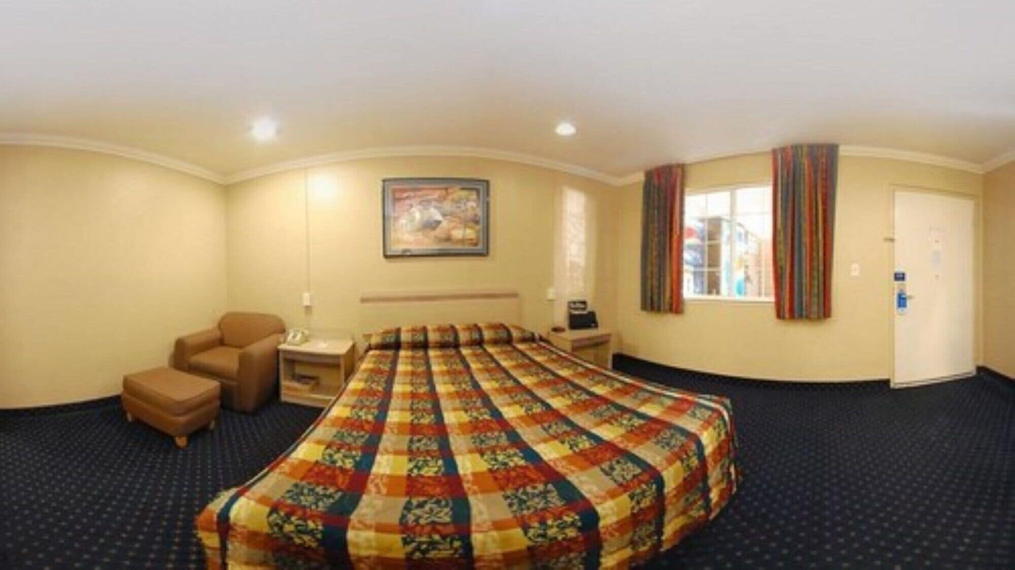 A hotel room with a large bed, a desk with a chair, a small sofa, a painting on the wall, and a window with curtains.
