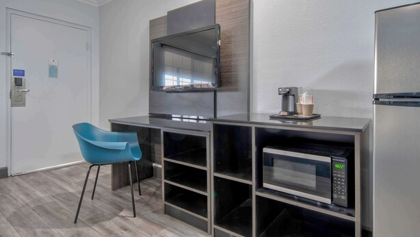 Uma kitchenette moderna com micro-ondas, cafeteira e uma cadeira azul.