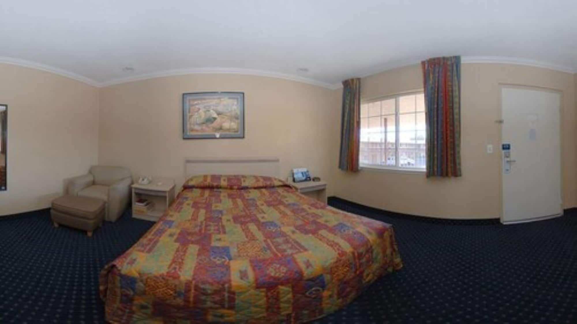 Quarto de hotel com uma cama grande, uma cadeira, uma mesa e uma janela com cortinas.