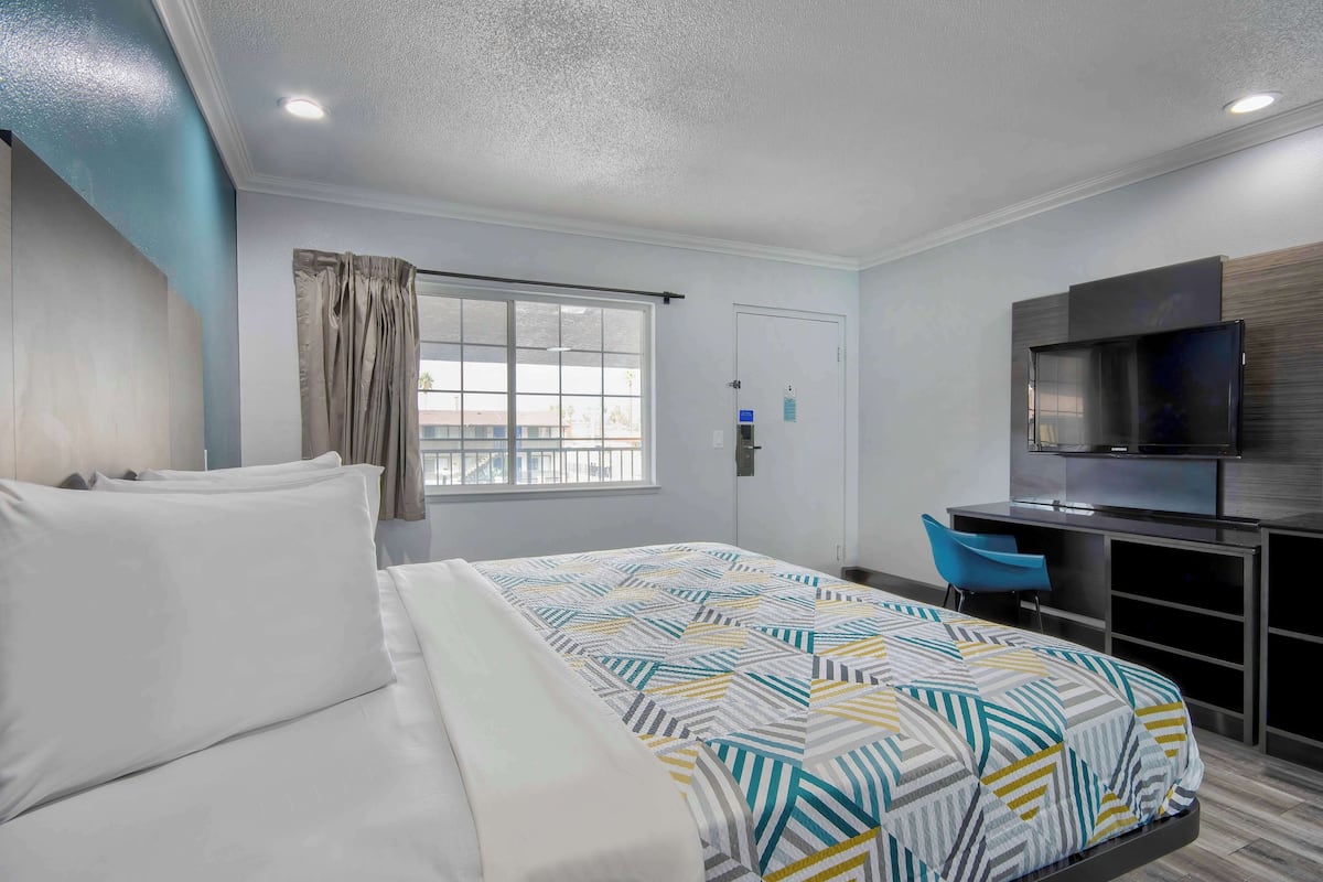 A hotel room with a bed, a desk with a chair, a TV, and a window with curtains.