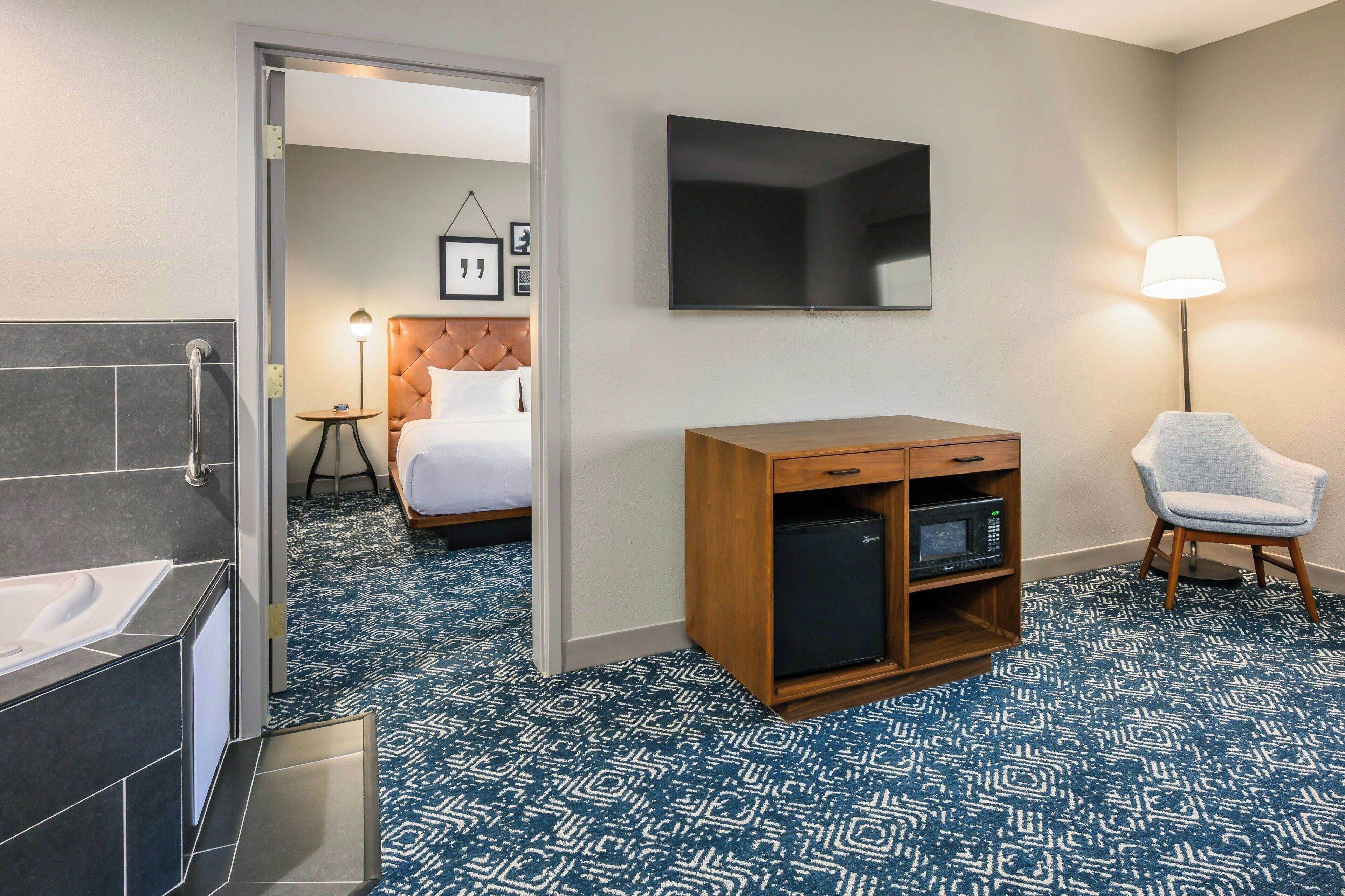 Une chambre d’hôtel avec une salle de bain, un lit, une télévision, une lampe et une petite table.
