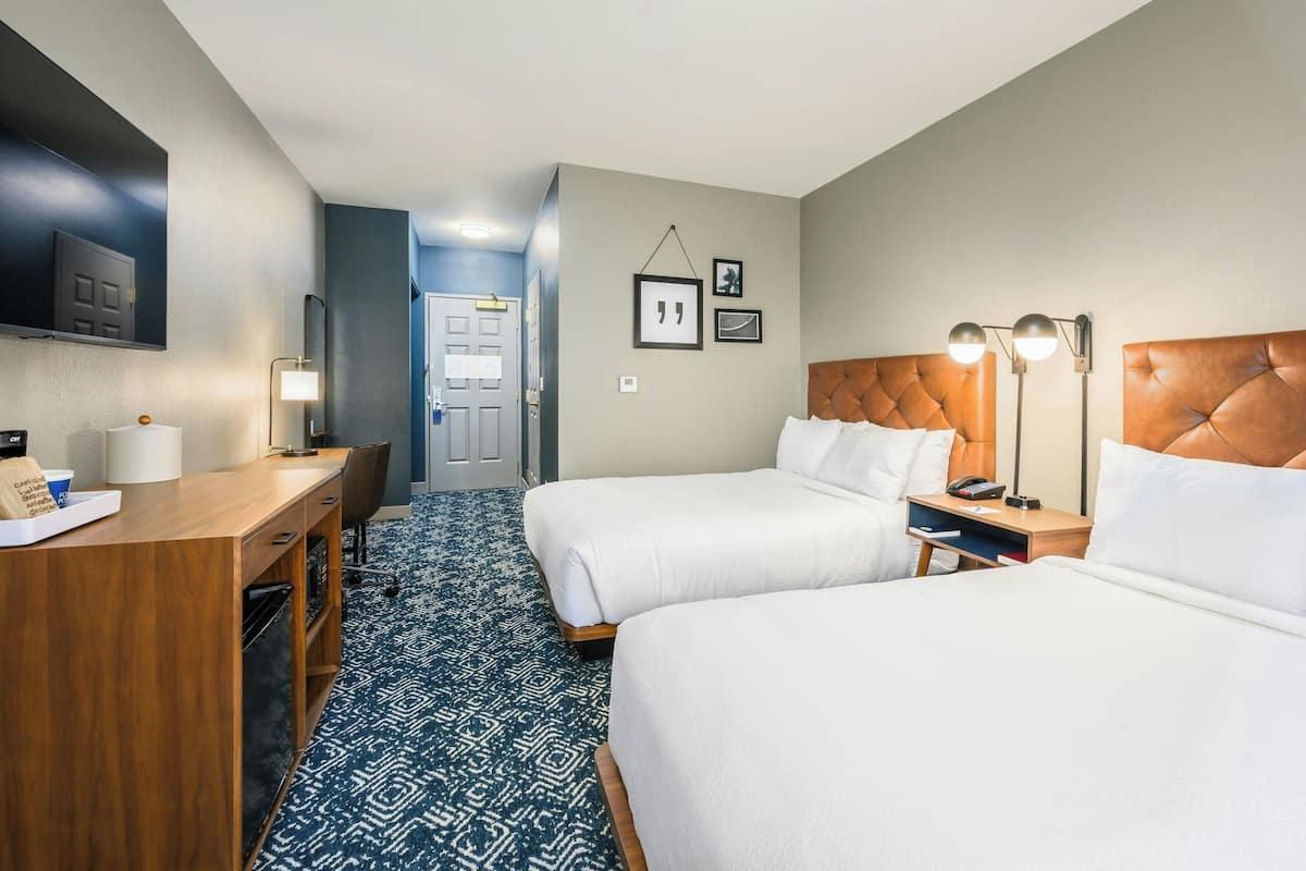 Hotellihuone, jossa on kaksi sänkyä, työpöytä, televisio ja kylpyhuone, joka näkyy avoimesta ovesta.