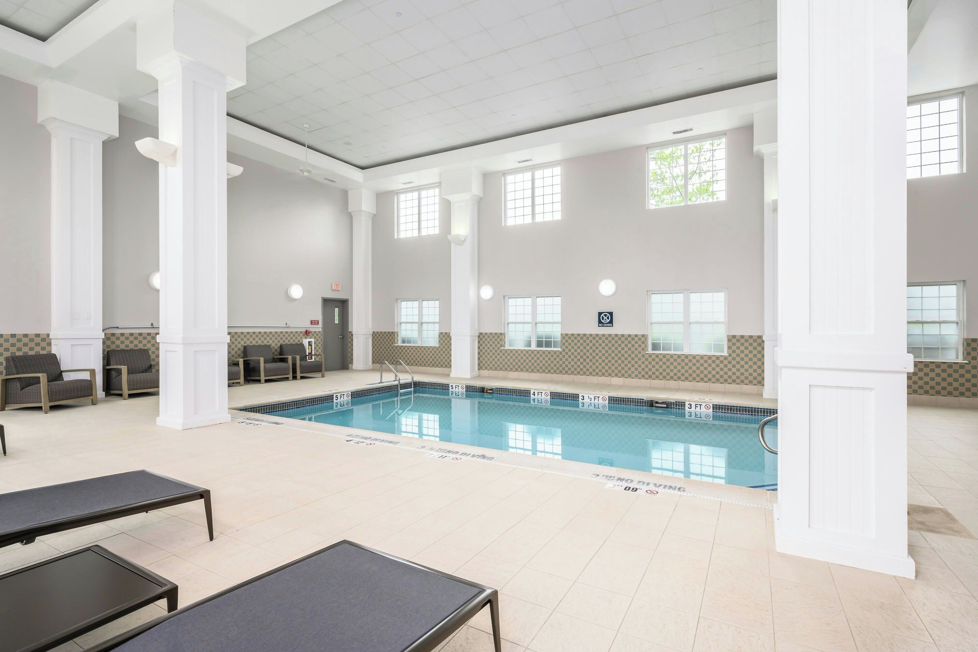 Uma grande piscina interior com divisórias bem demarcadas, rodeada por colunas brancas e paredes revestidas a azulejos bege.