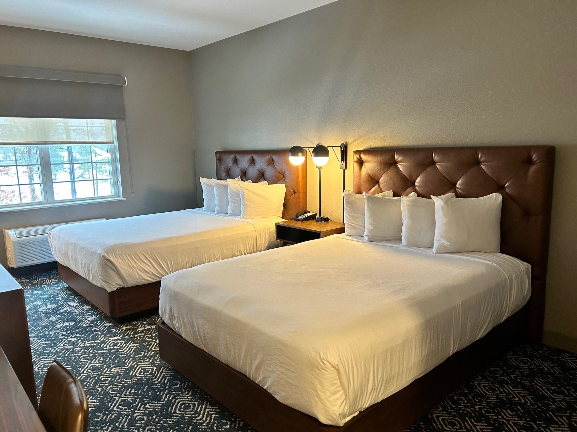 A hotel room with two beds, a large window, a desk, and a chair.