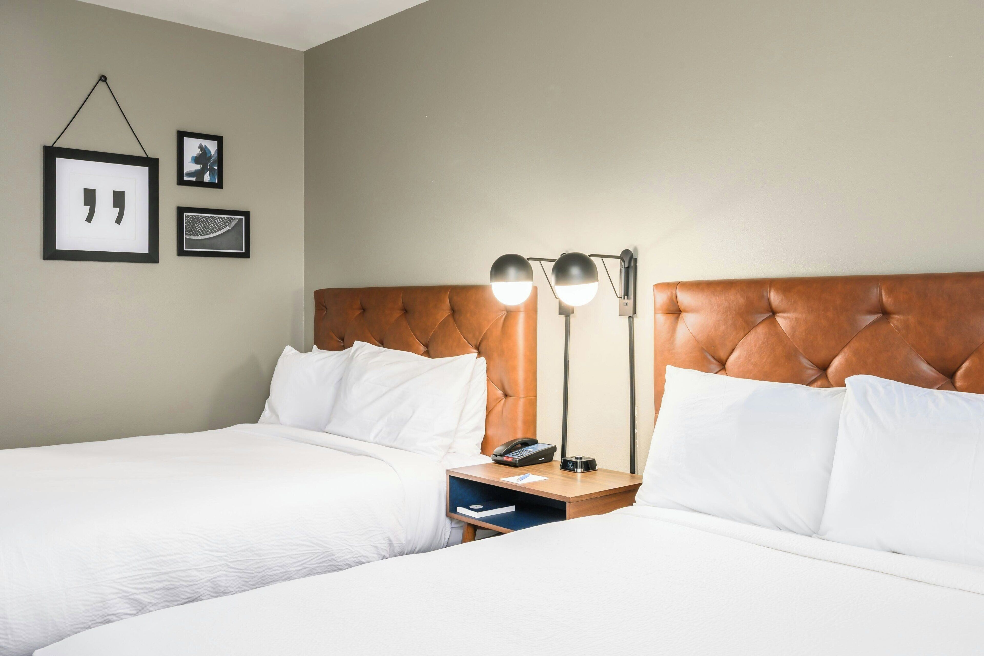 A hotel room with two beds, a wooden headboard, bedside tables with lamps, and framed pictures on the wall.
