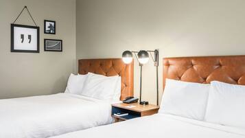 A hotel room with two beds, a wooden headboard, bedside tables with lamps, and framed pictures on the wall.