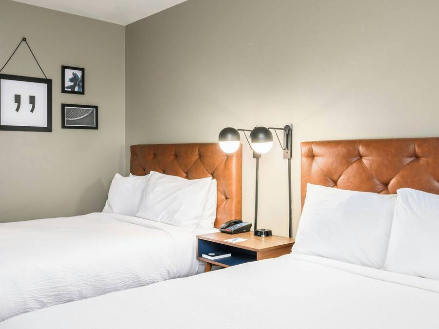 A hotel room with two beds, a wooden headboard, bedside tables with lamps, and framed pictures on the wall.