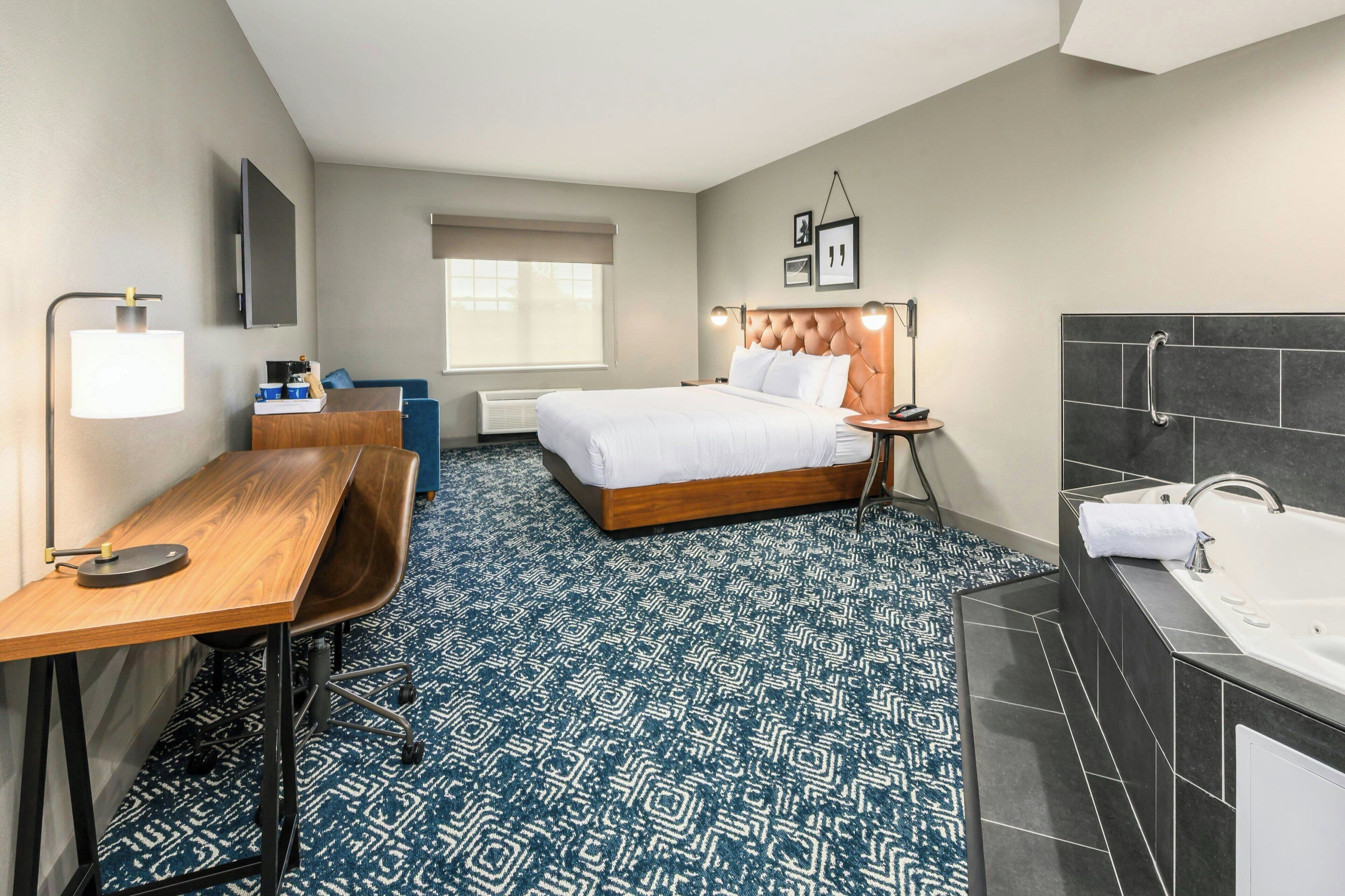 A hotel room with a bed, desk, chair, and a large bathroom with a bathtub.
