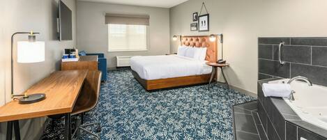 A hotel room with a bed, desk, chair, and a large bathroom with a bathtub.