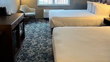 Une chambre d’hôtel avec deux lits, un bureau, une chaise, une fenêtre et une moquette à motifs.