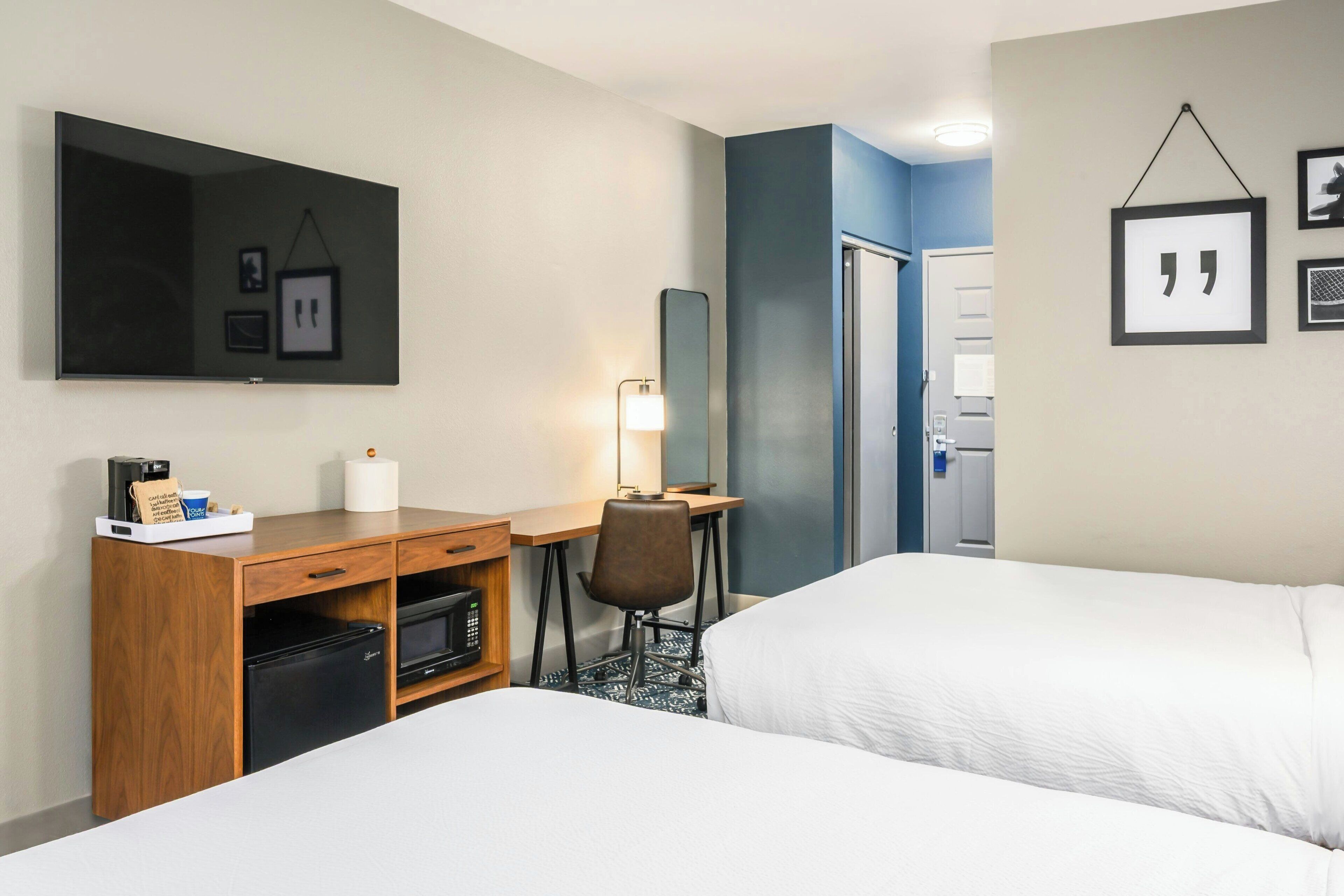 A hotel room with two beds, a desk with a computer, a chair, a TV, and a minibar.