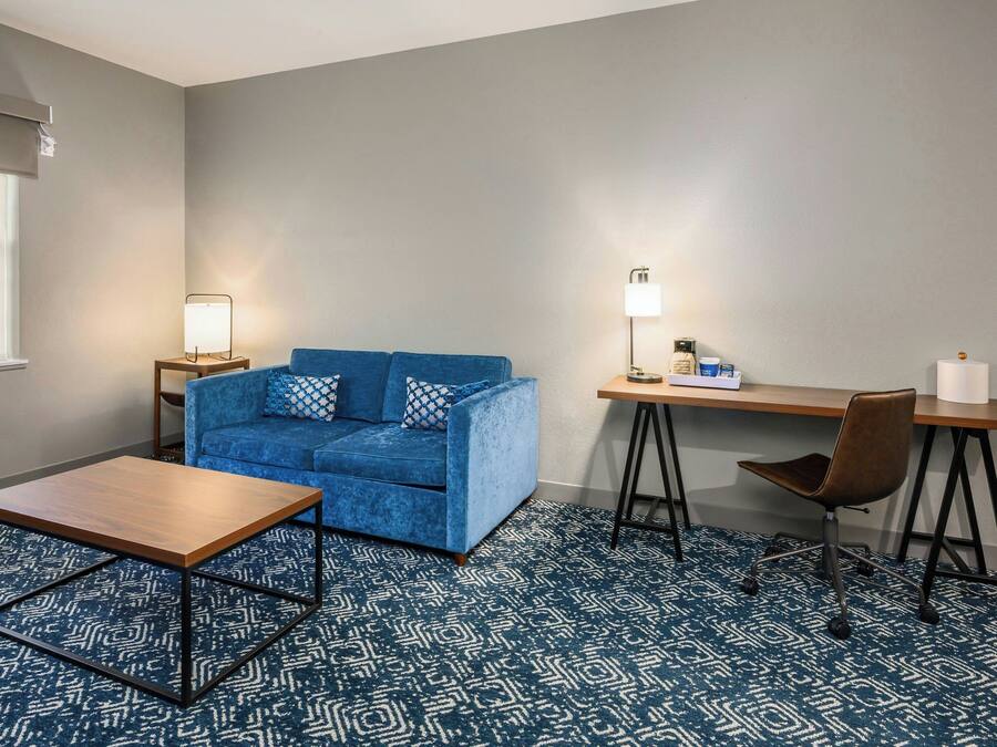 Una stanza con un divano blu, un tavolino in legno, una scrivania con una sedia e un tappeto decorato.