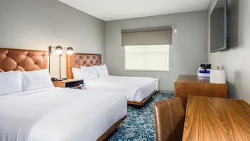 Quarto de hotel com duas camas, uma escrivaninha, uma cadeira, uma televisão e uma janela com vista.