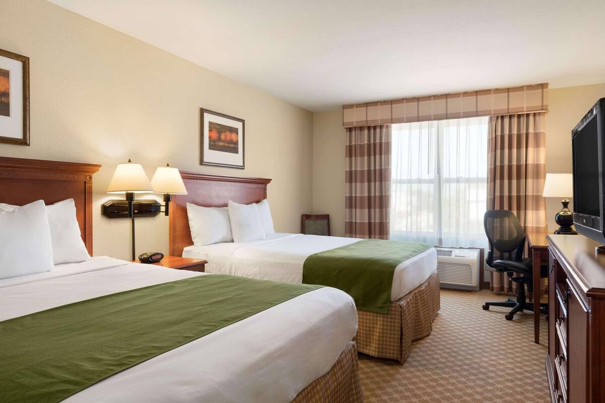 A hotel room with two beds, a desk, a chair, and a television.