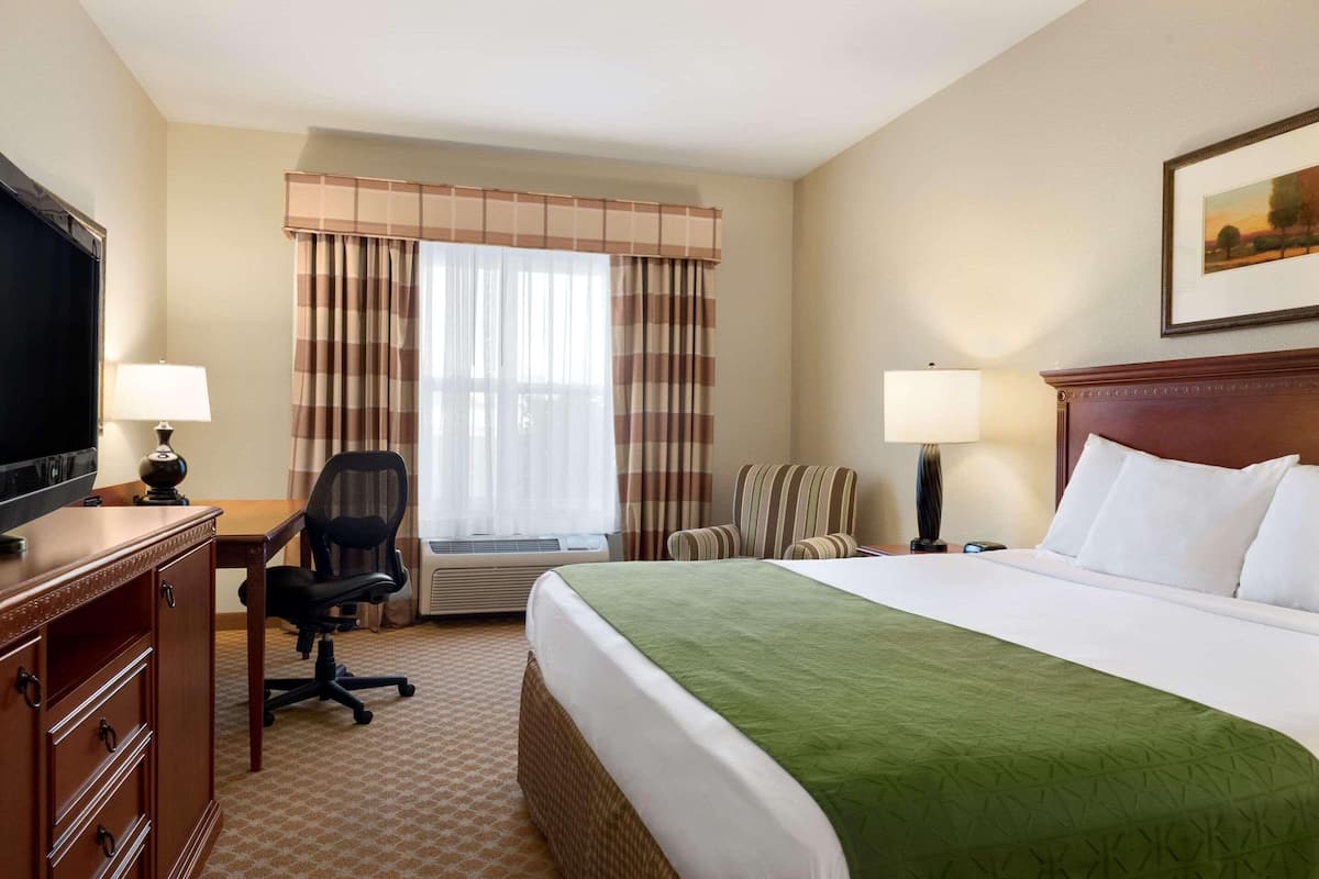A hotel room with a bed, desk, chair, television, and window with curtains.