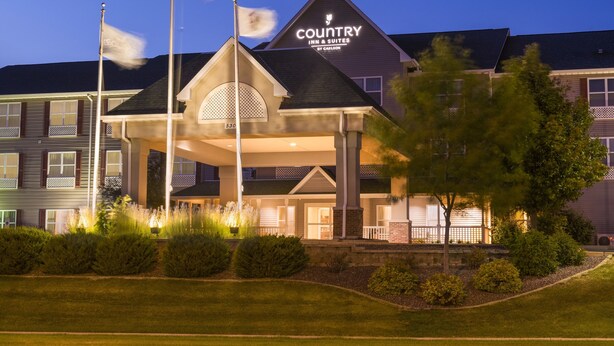 A hotel with a prominent sign reading "Country Inn & Suites by Carlson" and a flagpole with flags. - Country Inn & Suites by Radisson, Peoria North, IL (Peoria)