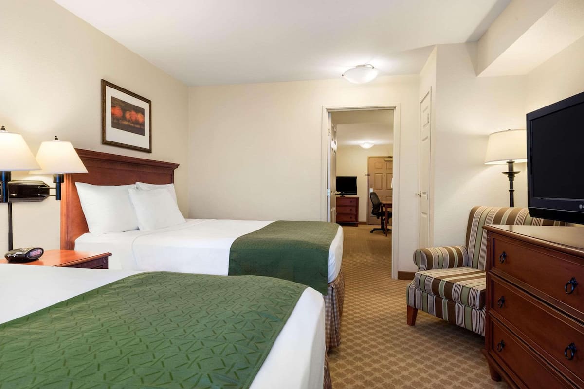 A hotel room with two beds, a television, a desk, and a chair.
